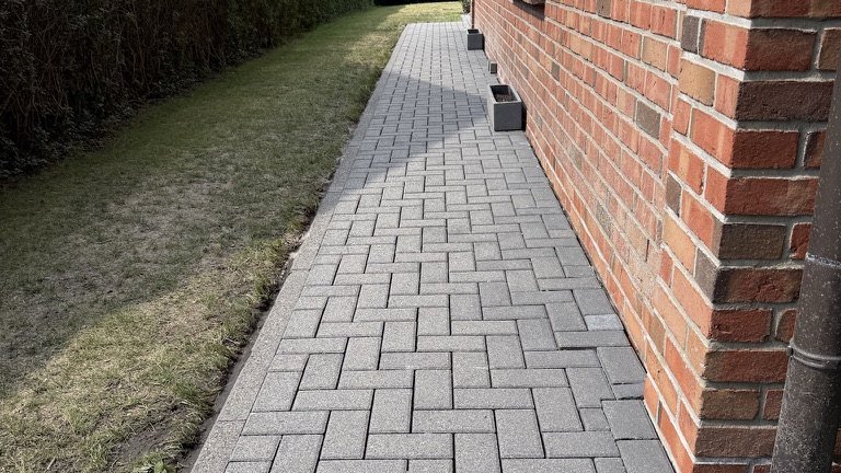 Fertig gereinigter Pflasterweg entlang einer Hauswand, Fugen sauber und gleichmäßig
