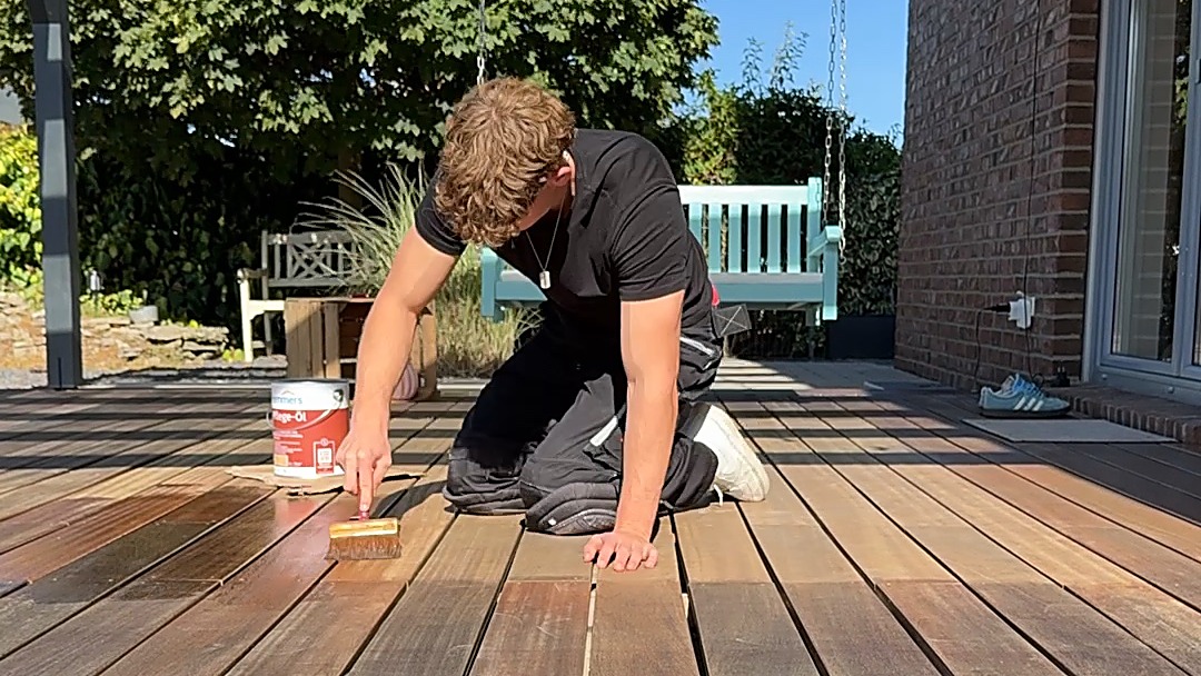 Beim Auftragen des Öls auf die Holzdielen, die frisch geölte Bahn deutlich dunkler als das Holz daneben