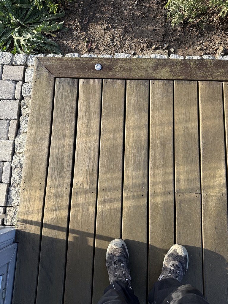 Ecke der Holzterrasse vor der Reinigung, die Platten dunkel und fleckig
