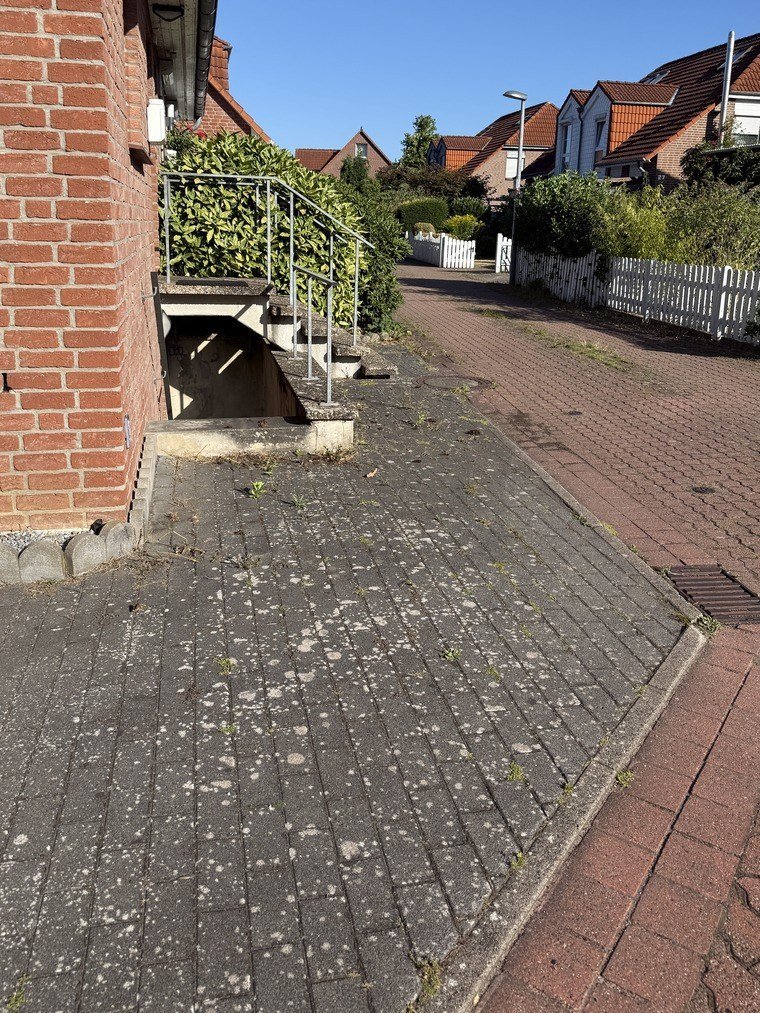 Gehweg an der Hausecke vor der Reinigung, das Pflaster stumpf und grau, Bewuchs an der Kante