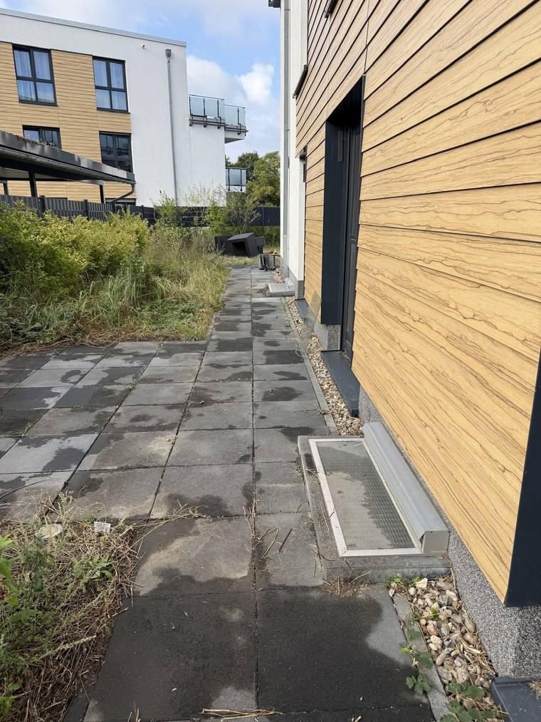 Plattenweg an einer Holzfassade vor der Reinigung, die Anthrazitplatten von hellen Ausblühungen überzogen