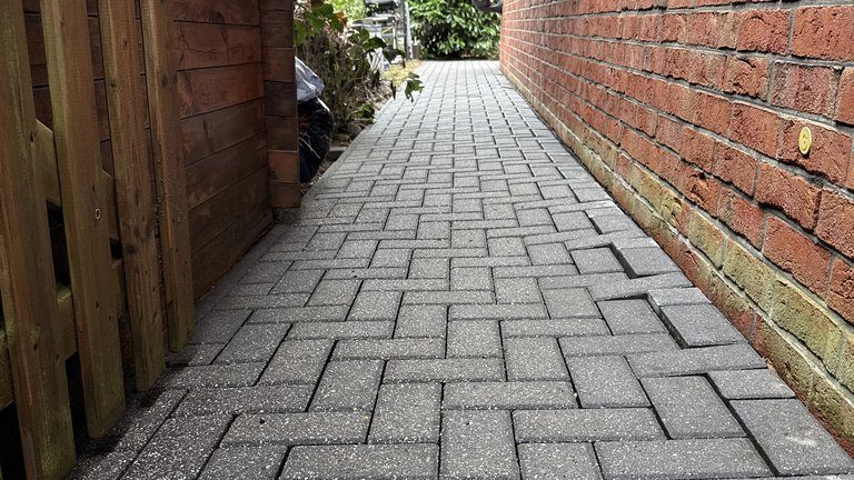 Fertig gereinigter Pflasterweg zwischen Holzzaun und Klinkerwand, das Fischgrätmuster wieder klar
