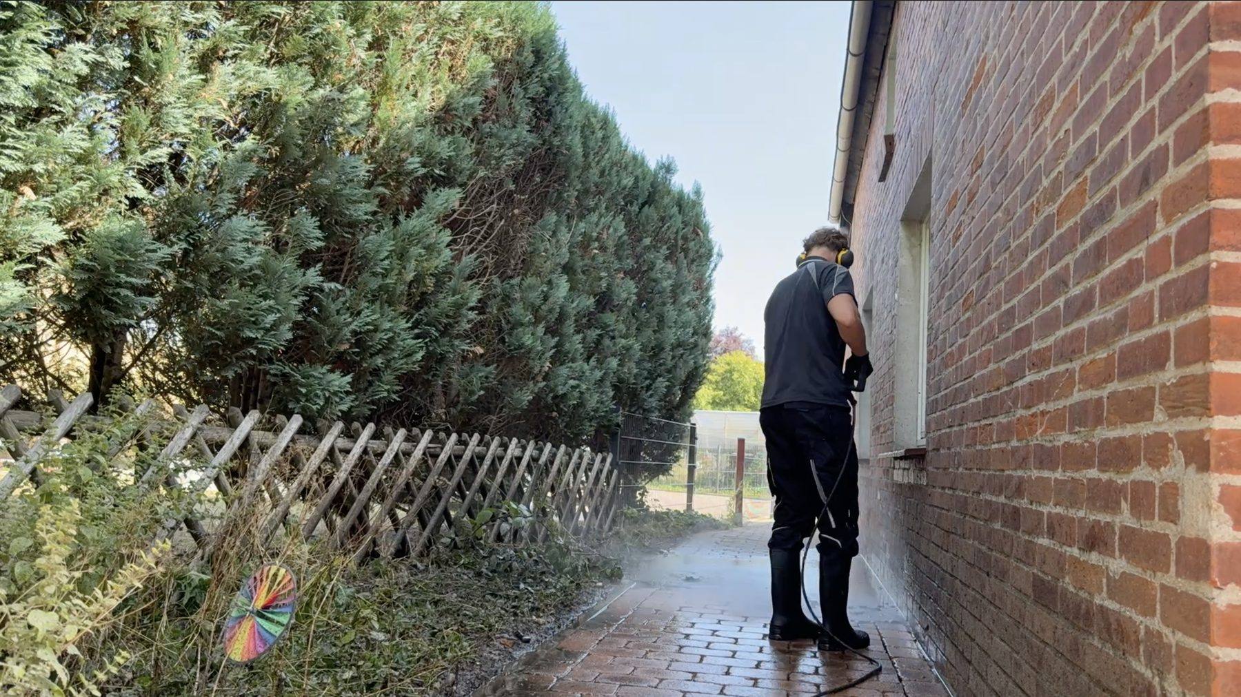 Schmaler Weg zwischen Hecke und Klinkerwand: Mika Rennert reinigt das Pflaster mit dem Hochdruckreiniger